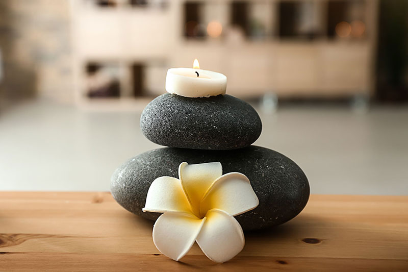 Spa stones, burning candle and flower on table